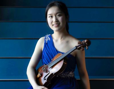 A woman in a blue dress sits holding a violin.