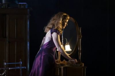 A woman in costume stands on a stage in front of a mirror