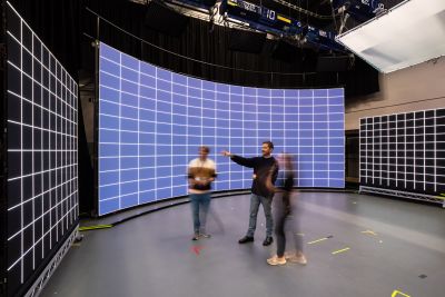 Three people standing in front of large LED screens in a film studio