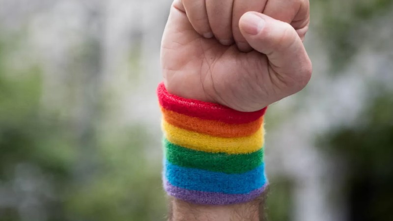 A person's raised fist wearing a rainbow wrist band