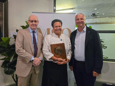 Three people stand in front of a banner, the woman in the middle holds an award