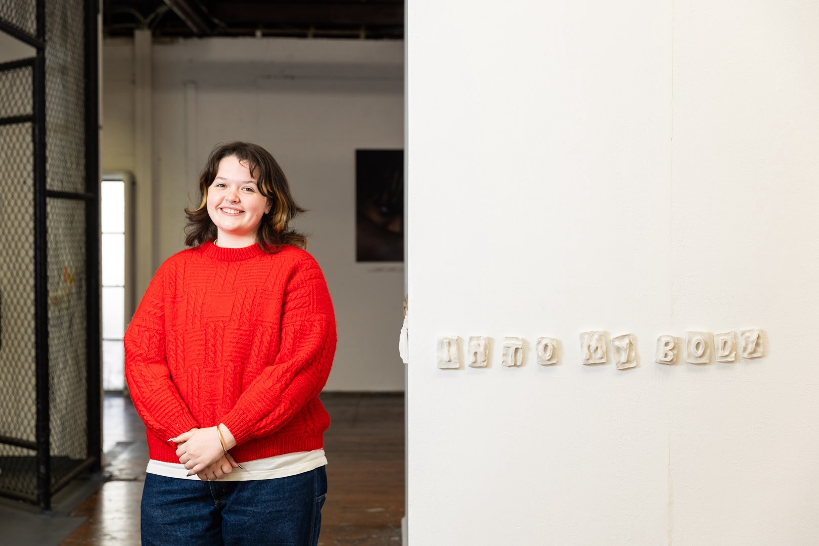 Artist stands next to an artwork that reads 'into my body'