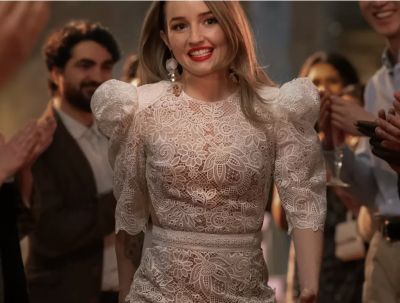 A woman in a white dress walks through a crowd smiling
