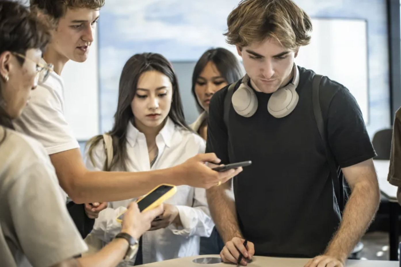 A group of students stand around a desk.