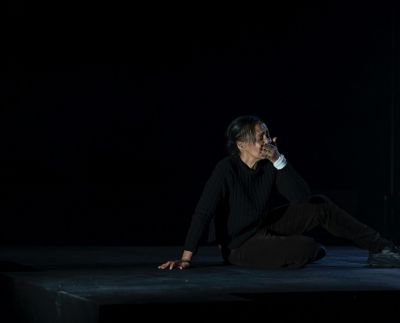 A woman sits on a dark stage looking upset