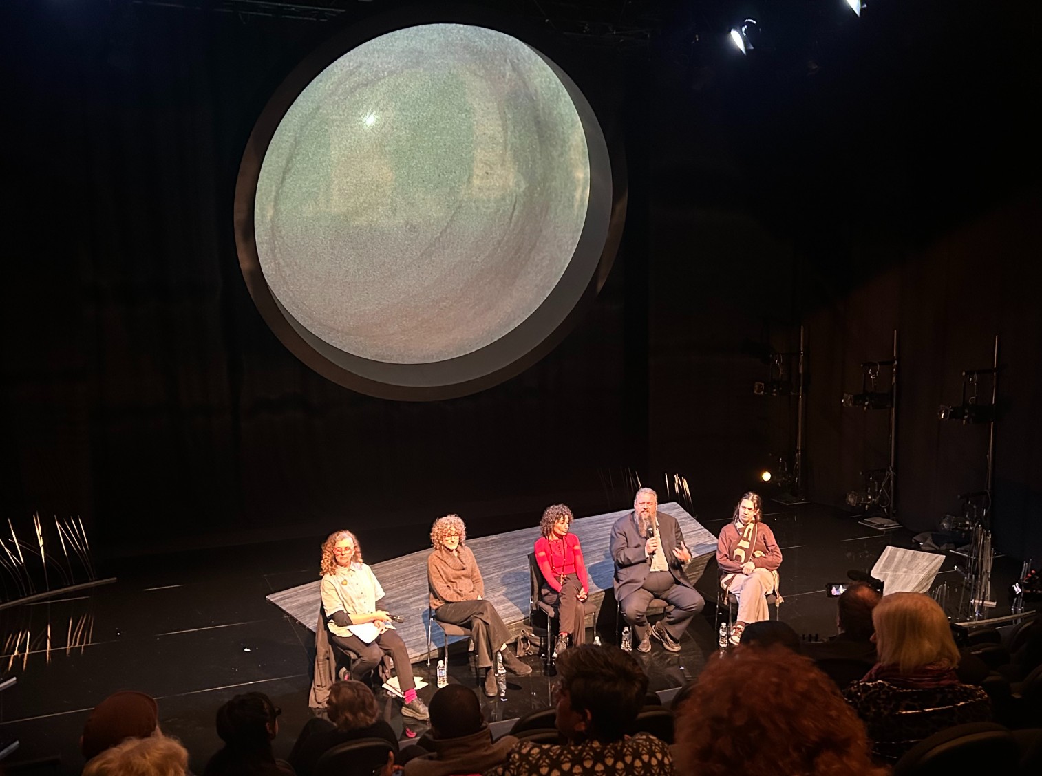 Five people on a panel sit on a dark stage talking