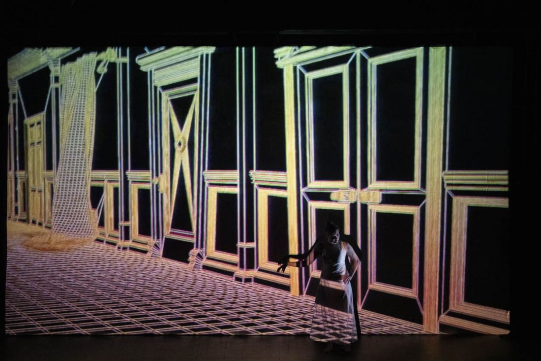 Girl posing in front of projection depicting a floor and wall of doors and openings