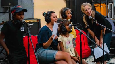 A group of children and adults record a song in a music studio