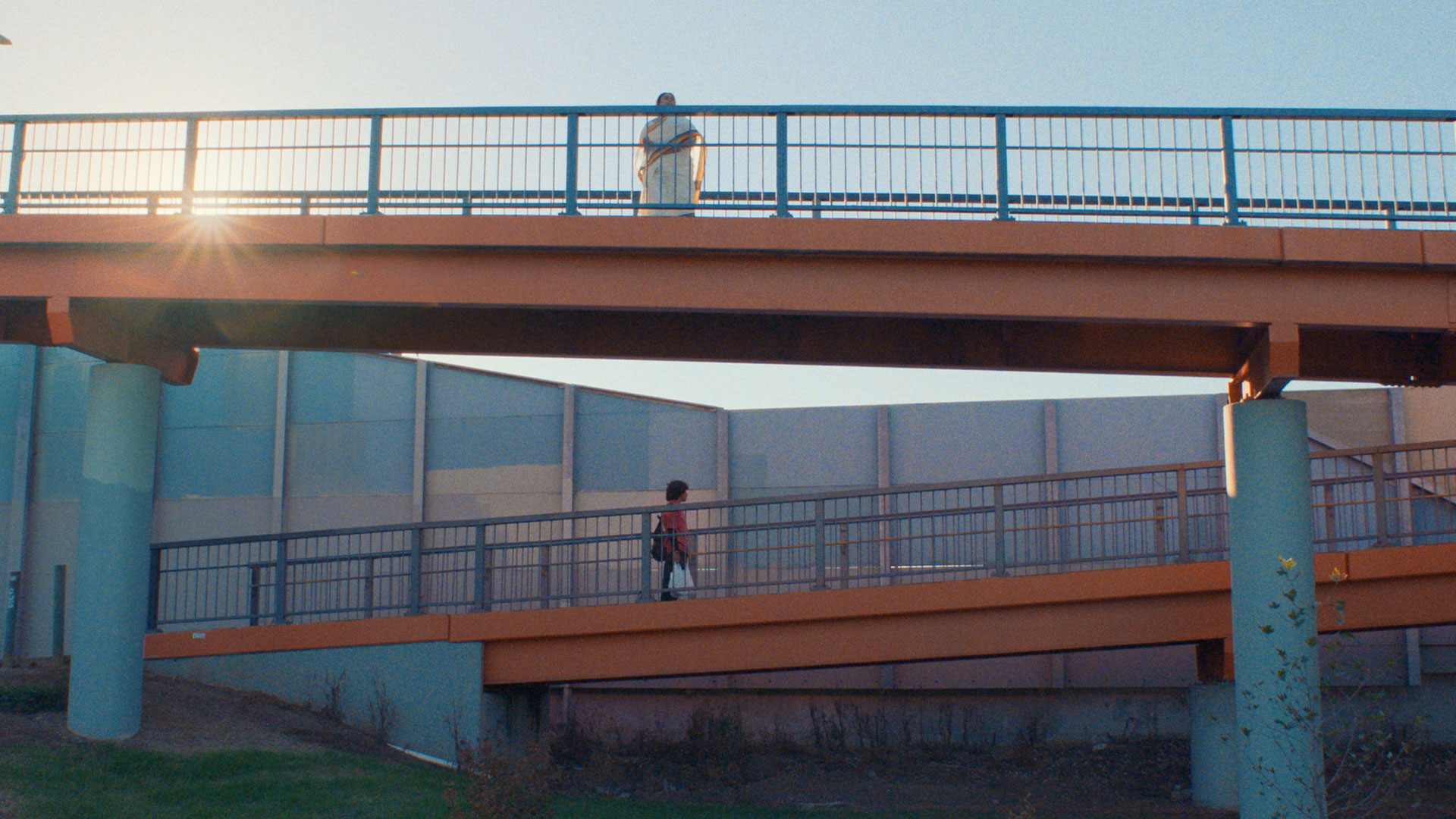 Two people walk across parallel bridges with the sun shining