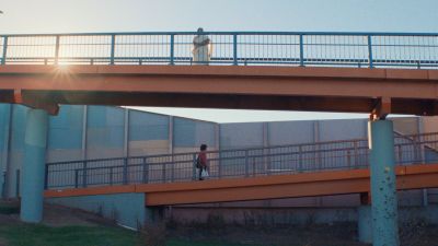 Two people walk across parallel bridges with the sun shining