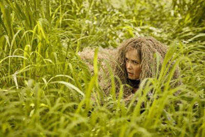 A woman dressed in camouflage hides in grassland