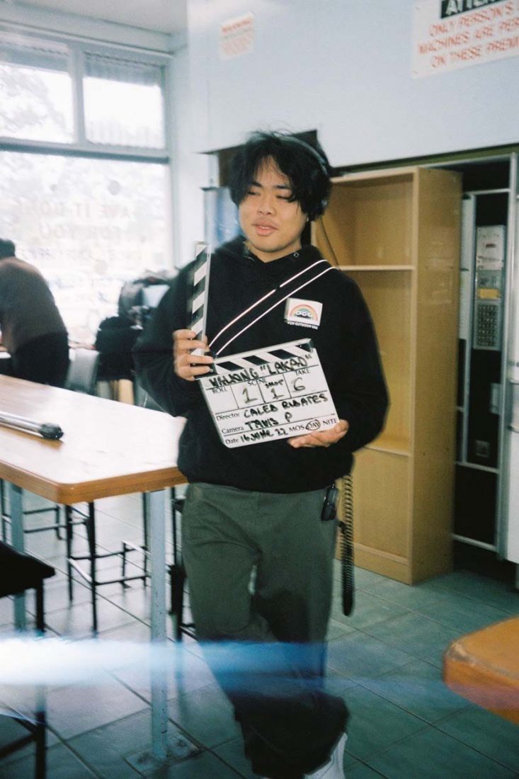 Filmmaker Caleb Ribates on set holding a clapperboard wth headphones on.