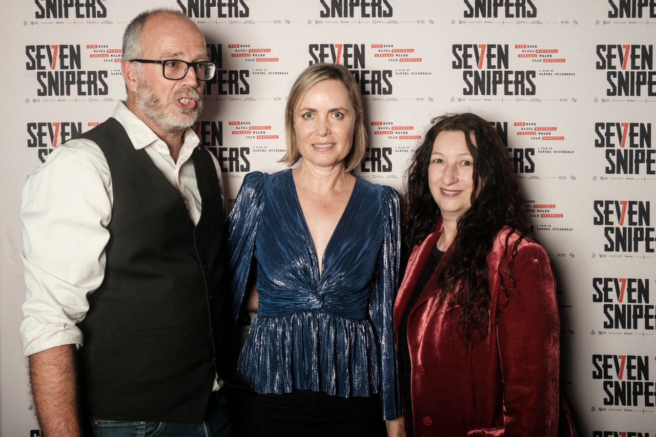 Three people stand in front of a promotional backdrop for a film