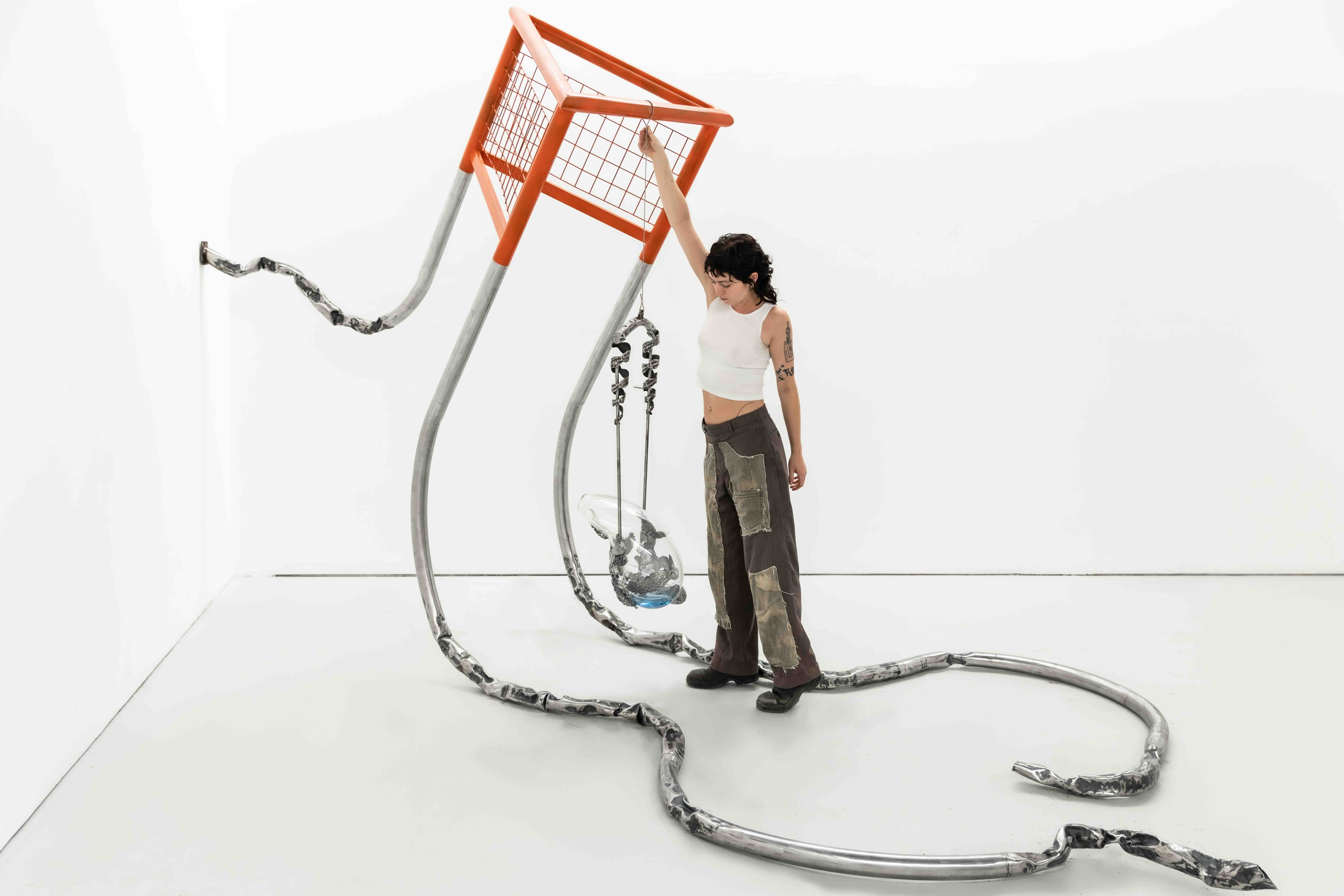 A person holds on to a bright orange hanging artwork in a white gallery space