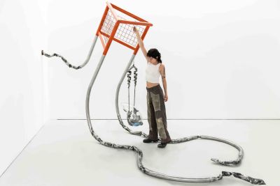 A person holds on to a bright orange hanging artwork in a white gallery space