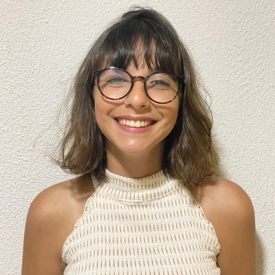 Luiza is wearing glasses and a white top. She is smiling at the camera.